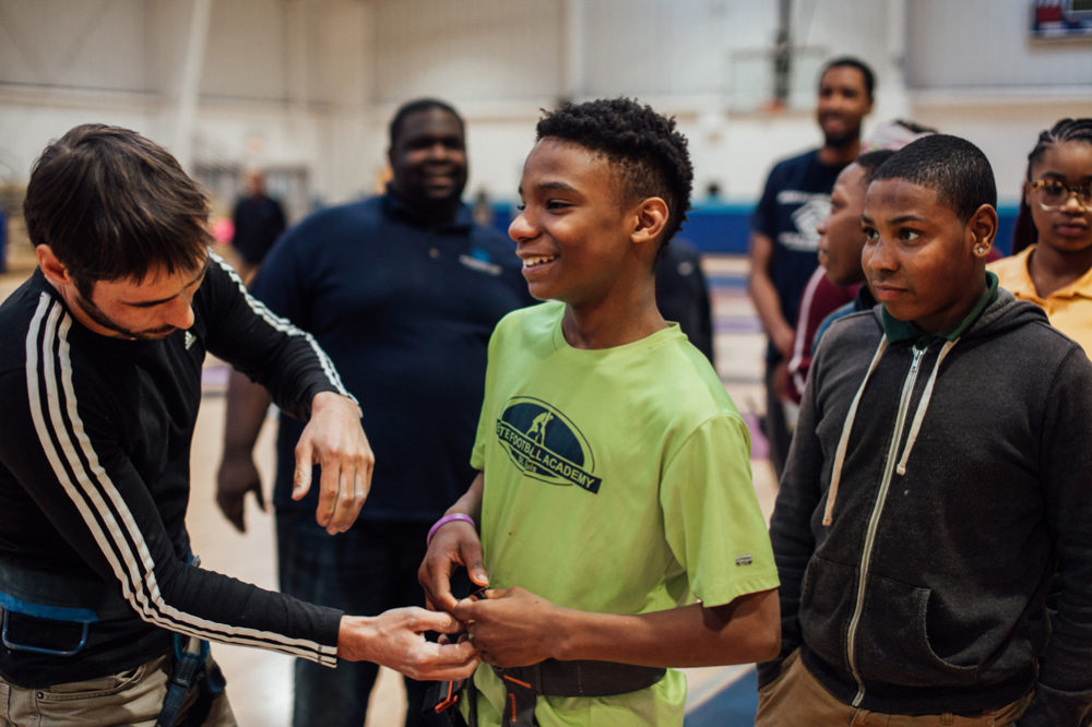 Kevin helps fit a climbing harness on a Boys and Girls club member.