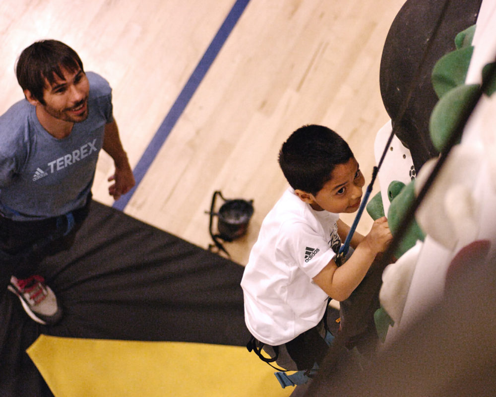 Kevin Jorgeson watches as a boys and girls club member climbs a new 1Climb wall for the first time.